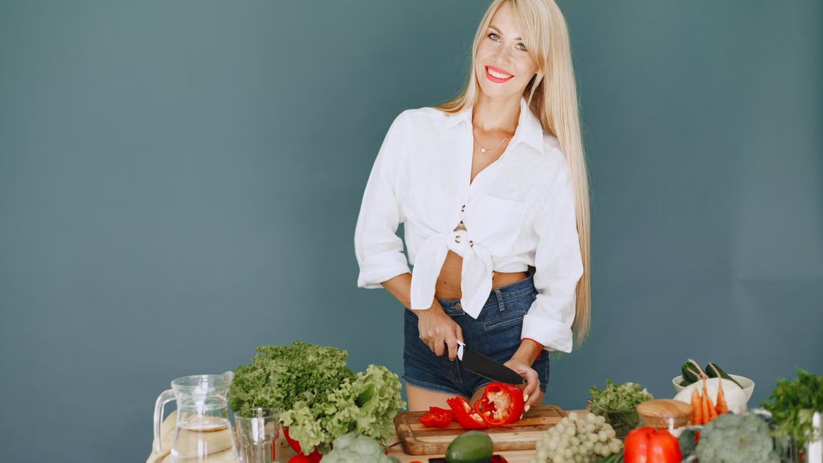 A smiling blonde woman chops vegetables, promoting healthy eating and lifestyle.